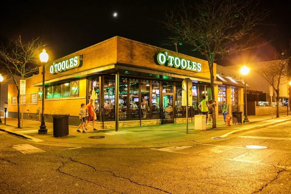 O'Toole's corner bar at night: green neon O'TOOLES signs, warm amber street lights and glowing windows on an empty street corner.